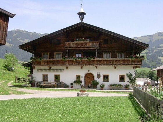 Malernhof Kitzbühel im Sommer Traditionelles Alpenhaus aus Holz und weißem Putz mit Blumenbalkonen vor bewaldeten Bergen.