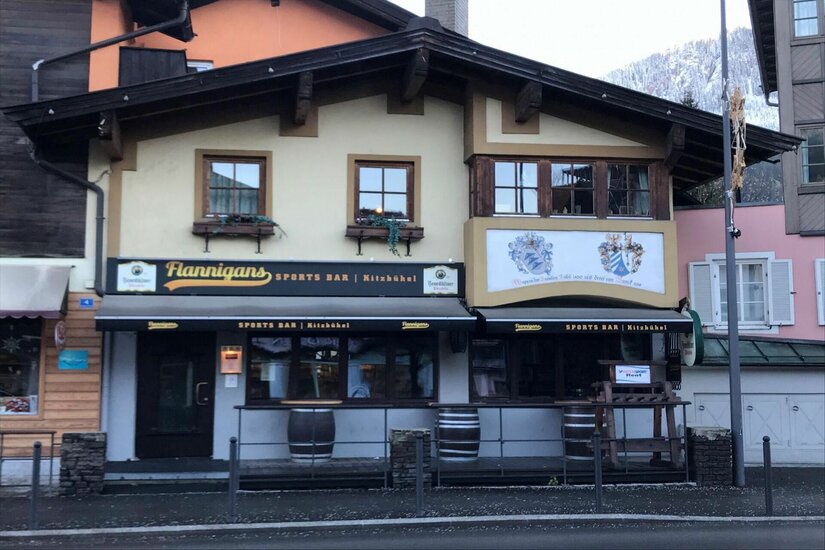 Flannigans Sports Bar Kitzbühel Außenansicht der Flannigans Sports Bar in Kitzbühel mit dunklen Markisen und Holzfassade.