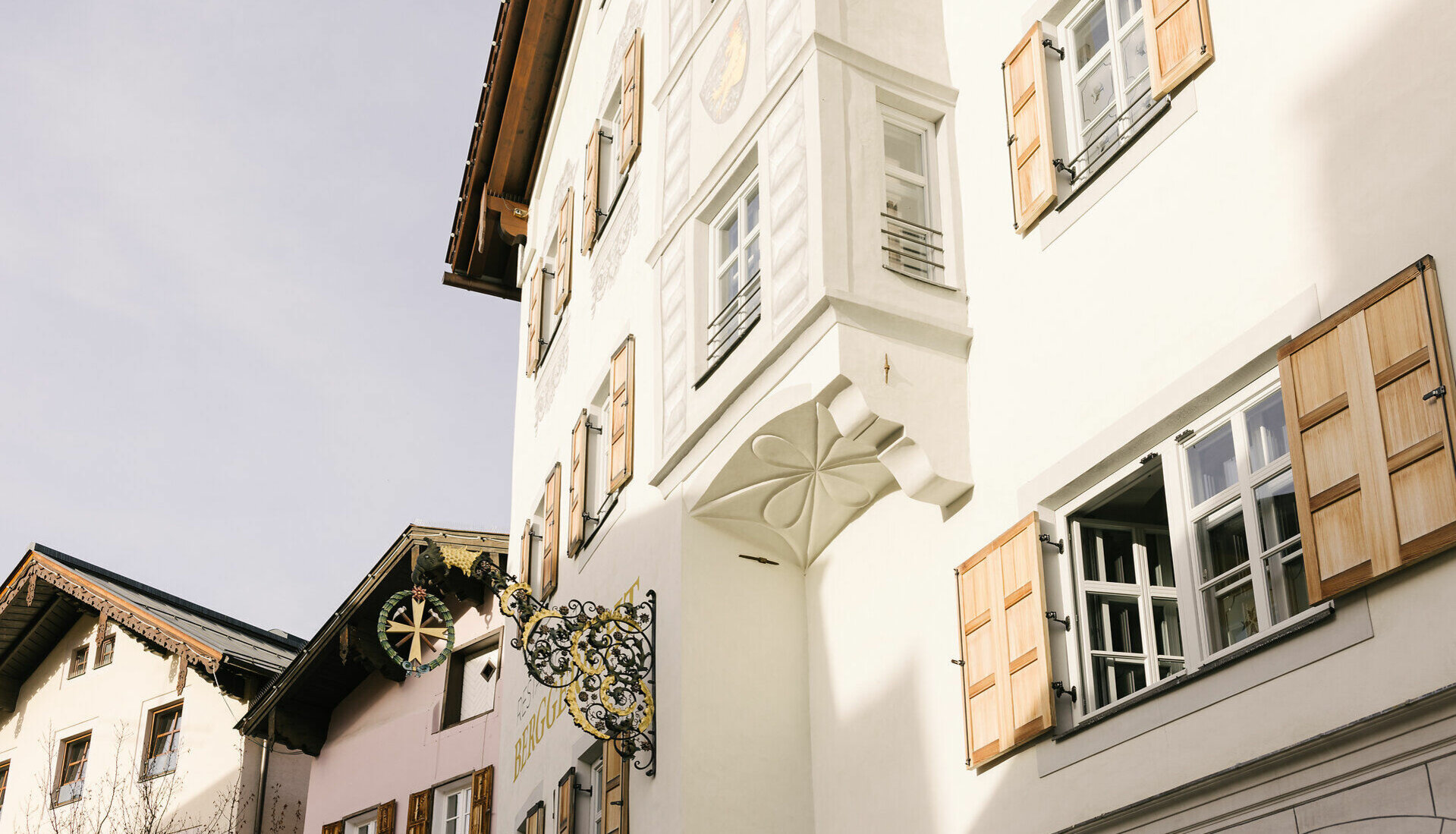 Ein charmantes Stadtbild mit traditionellen Holzbalkonen und einem kunstvollen Wirtshausschild in Kitzbühel.