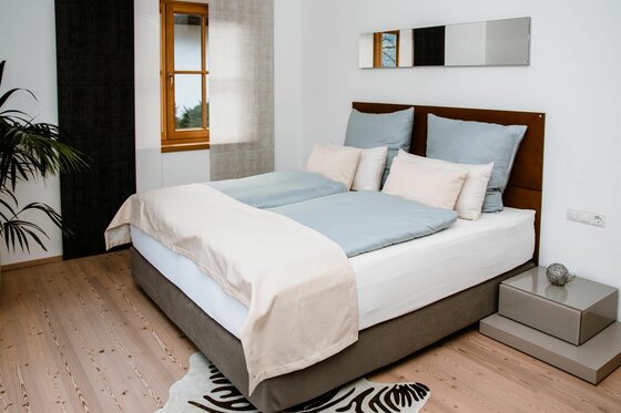 Schlafzimmer Residenz am Berg 3 Modernes Doppelbett mit hellblauer Bettwäsche in einem hellen Zimmer mit Holzboden.