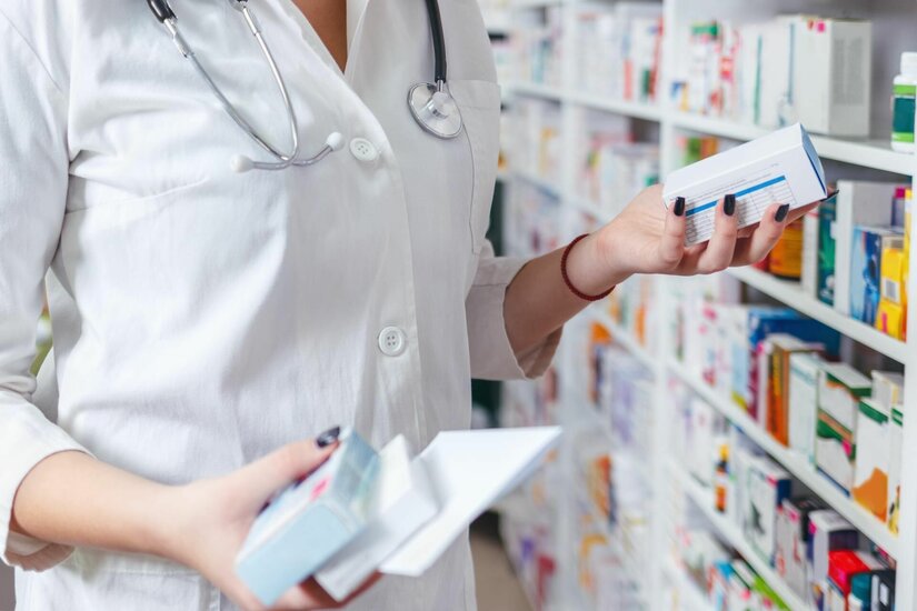 Service in der Rosenapotheke Person im weißen Kittel hält Medikamentenschachteln vor einem Apothekenregal.