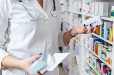 Service in der Rosenapotheke Person im weißen Kittel hält Medikamentenschachteln vor einem Apothekenregal.