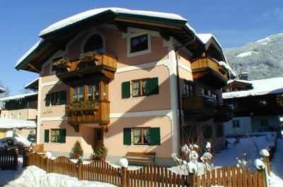 Haus Savoy im Winter Mehrstöckiges alpines Wohnhaus mit Holzfassadenelementen und schneebedecktem Dach unter blauem Himmel.