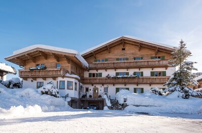Apartment Foidl im Winter Alpines Holzhaus mit Balkonen im Schnee unter blauem Himmel.