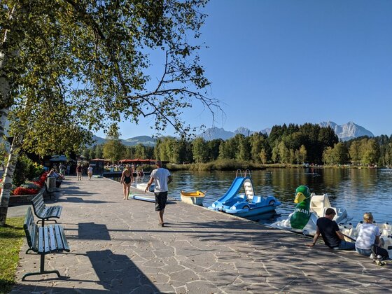 Uferpromenade am Schwarzsee Gepflasterte Uferpromenade am Schwarzsee mit Tretbooten, Bänken und Blick auf bewaldete Berge.