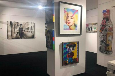 Walentowski Gallerie Jochberg Eine Kunstgalerie mit mehreren bunten Gemälden und Fotografien an den Wänden. Der Boden ist schwarz und die Beleuchtung ist hell und freundlich.