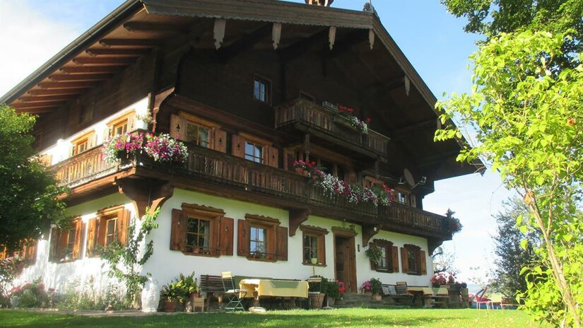 Traditionelles Alpenhaus mit Blumenbalkonen und weißer Fassade unter blauem Himmel.