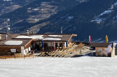 Berghütte Wagstättalm mit Außenterrasse und Holztischen direkt an einer Skipiste im Winter.