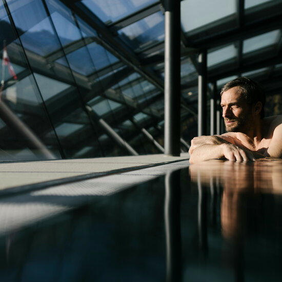 Ein Mann entspannt in einem modernen Pool mit großen Fenstern, die einen Blick auf die Berge bieten.