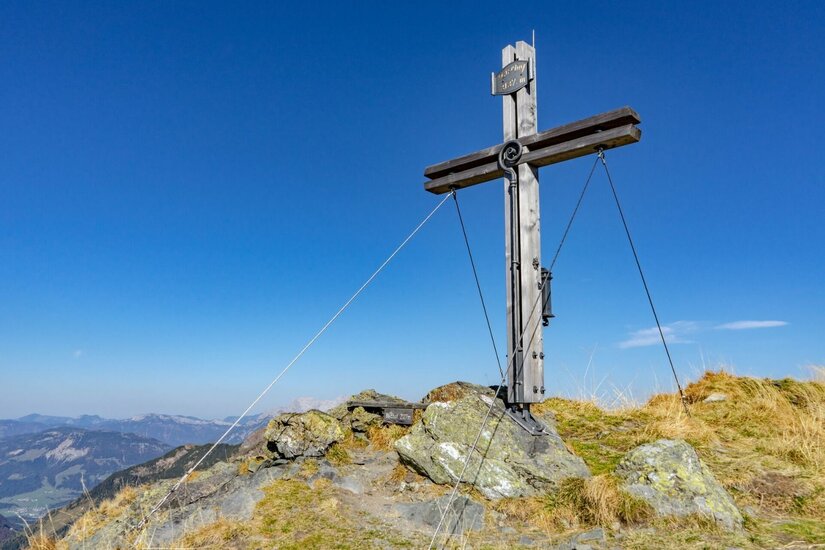 Gipfelkreuz am Bischof Ein hölzernes Gipfelkreuz auf einem felsigen Berggipfel vor blauem Himmel.