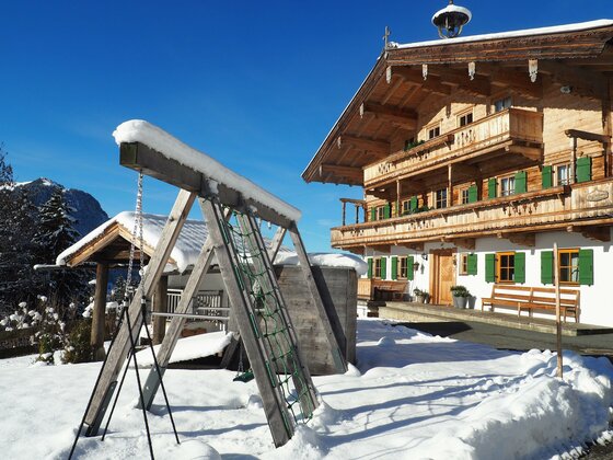 P1010534 Ein charmantes Chalet im Schnee mit grünen Fensterläden. Neben dem Haus steht eine Schaukel in der verschneiten Landschaft.