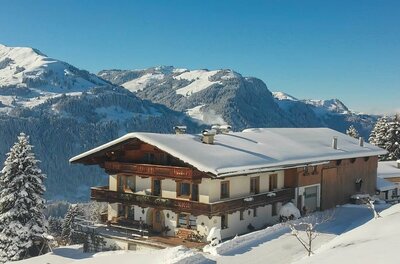 Hof Hamoos im Winter Ein schneebedeckter Bauernhof mit Holzbalkonen vor einer alpinen Bergkulisse im Winter.