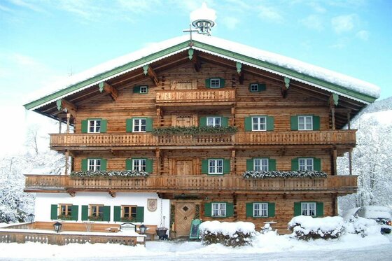 Mehrstöckiges Holzhaus mit grünen Fensterläden und schneebedecktem Dach vor winterlicher Kulisse.