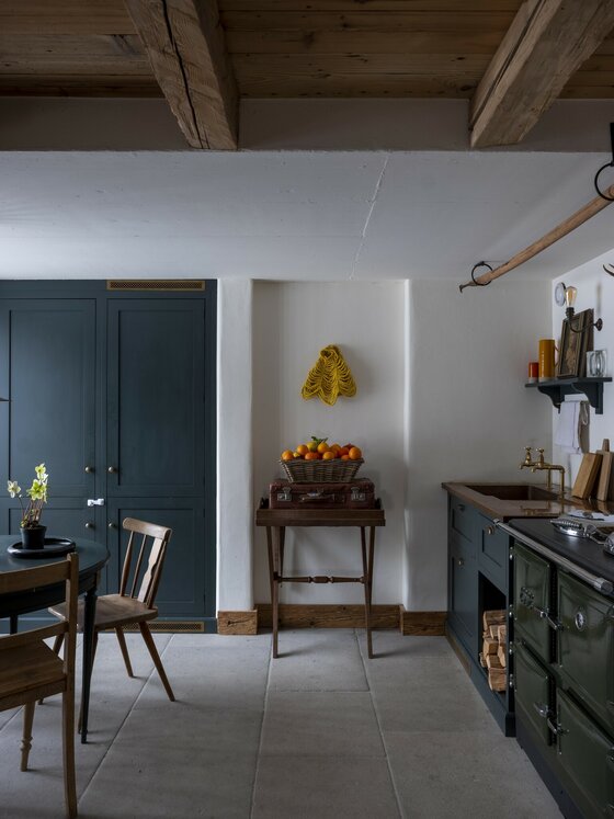 Küche im Green Chalet Rustikale Küche mit dunklen Schränken, einem Holzherd, Steinfußboden und Holzbalkendecke.