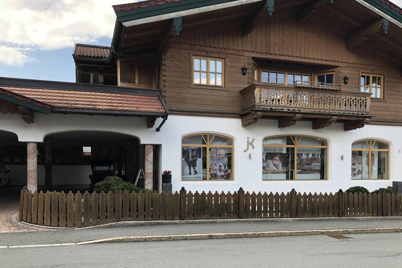 Pelzkunst Geschäftshaus Zweistöckiges Gebäude im alpinen Stil mit Holzobergeschoss, Balkon und Schaufenstern hinter einem Holzzaun.