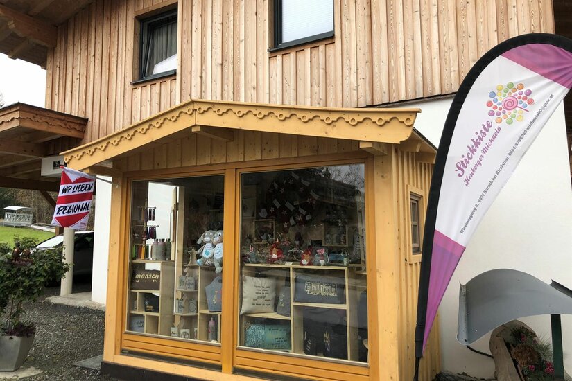 Stickkiste Verkaufsstand Kleiner Holzpavillon mit Glasfront und ausgestellten Handwerkswaren vor einem Holzhaus.