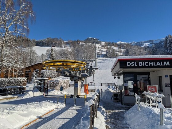 Talstation des Sessellifts Bichlalm in einer verschneiten Winterlandschaft unter blauem Himmel.