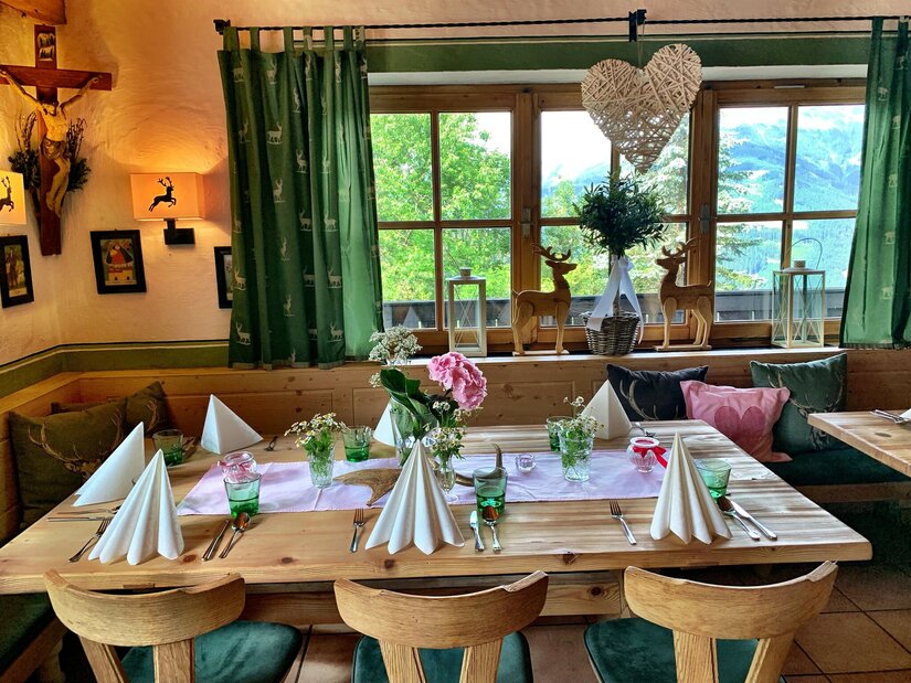 Gedeckter Holztisch in einer rustikalen Gaststube mit Blick durch ein Fenster auf die Berge.