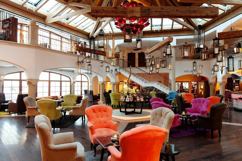 Marktplatzbar im Hotel Große Hotellobby mit bunten Sesseln, Holzbalkendecke und zahlreichen hängenden Laternen.