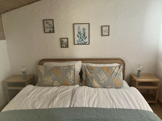 Schlafzimmer in Hannas Home Doppelbett mit gemusterten Kissen, zwei Nachttischen und botanischen Bildern an einer weißen Wand.