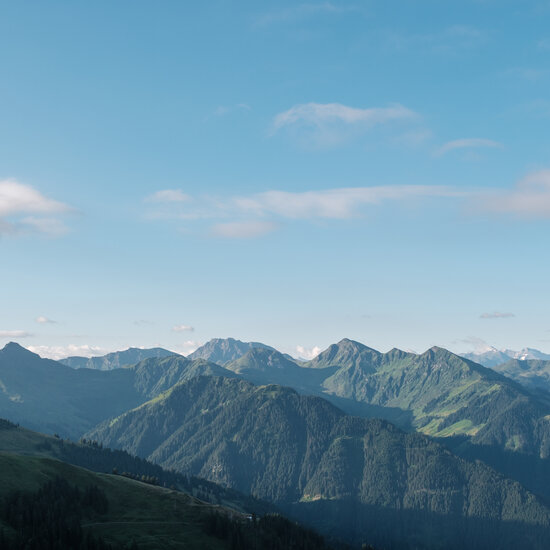 Eine atemberaubende Berglandschaft mit sanften Hügeln und schneebedeckten Gipfeln unter einem klaren blauen Himmel.