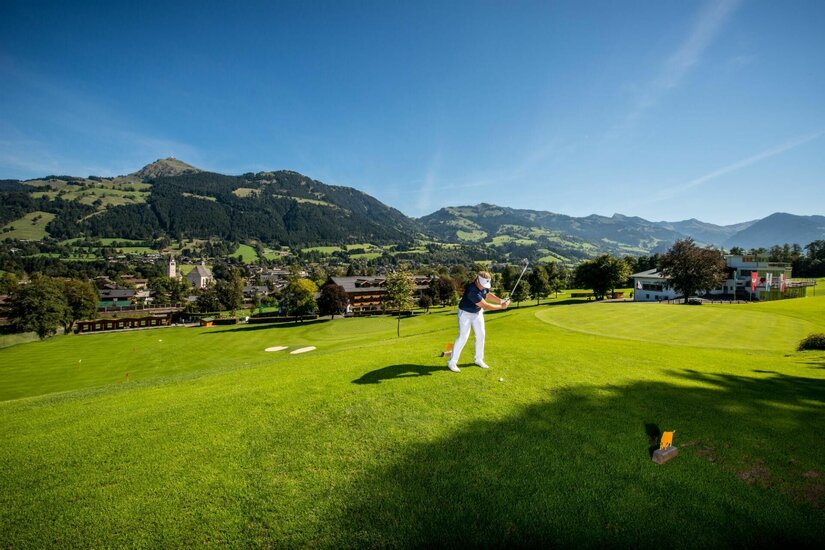 Golfplatz mit Bergpanorama Eine Person beim Golfschlag auf einem grünen Rasenplatz vor einer Bergkulisse.
