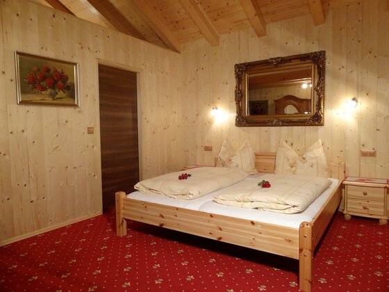 Doppelbett aus hellem Holz in einem Zimmer mit Holzvertäfelung und rotem Teppichboden.