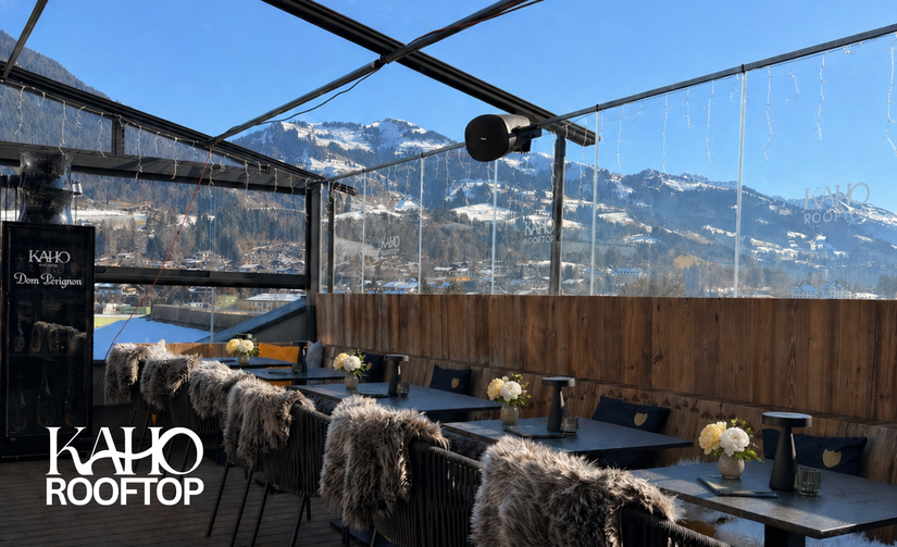 Moderne Dachterrasse mit Tischen, Stühlen mit Fellauflagen und Blick auf schneebedeckte Berge.
