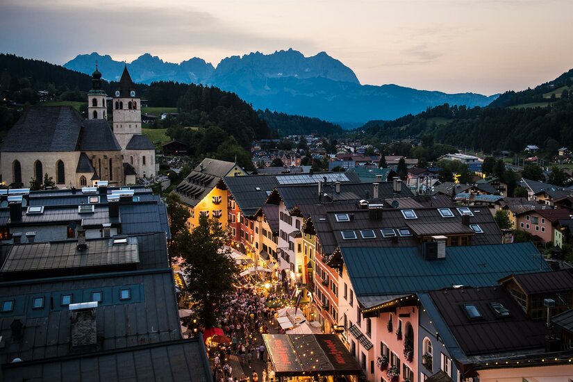 Blick über die Dächer von Kitzbühel mit Kirche und Gebirgskette im Hintergrund bei Dämmerung.