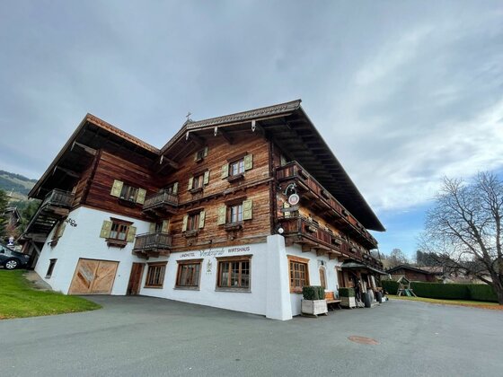 Alpines Gasthaus am Kitzbüheler Horn Mehrstöckiges alpines Gasthaus mit weißem Erdgeschoss und dunkler Holzfassade in den Obergeschossen.