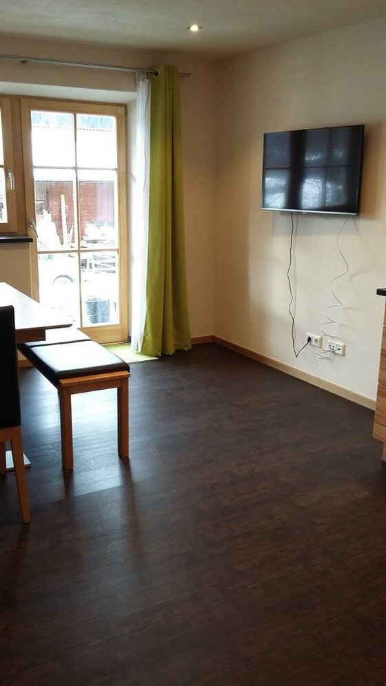 Wohnbereich im Biohof Foidl Wohnbereich mit dunklem Boden, Esstisch, Sitzbank und wandmontiertem Fernseher.