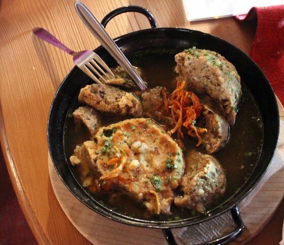 Kaspressknödel in der Pfanne Kaspressknödel in einer dunklen Brühe serviert in einer schwarzen Eisenpfanne auf einem Holztisch.