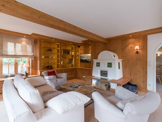 Wohnzimmer im Haus Schmidt Wohnzimmer mit hellen Sofas, Holzverkleidung an Wänden und Decke sowie einem weißen Kachelofen.