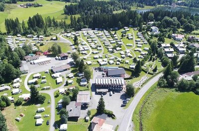 Campingplatz Schwarzsee Stellplätze Luftaufnahme eines Campingplatzes mit zahlreichen Wohnwagen, Gebäuden und angrenzendem Wald am See.