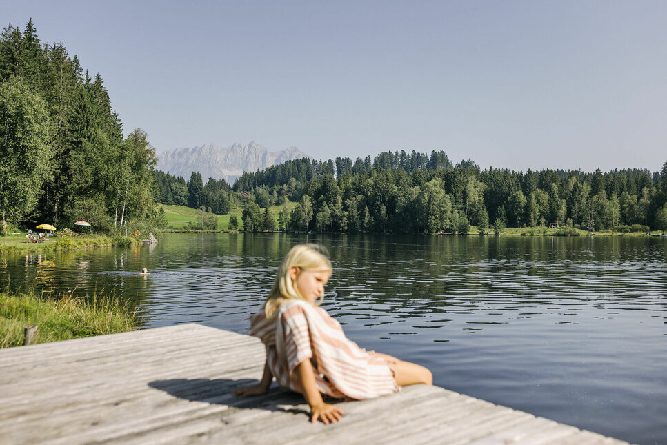 A little girl is sitting on the shore of Lake Schwarzsee