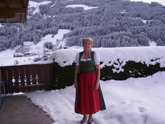 Frau in Tracht vor Haus Schuh Frau in Tracht vor verschneiter Bergkulisse.