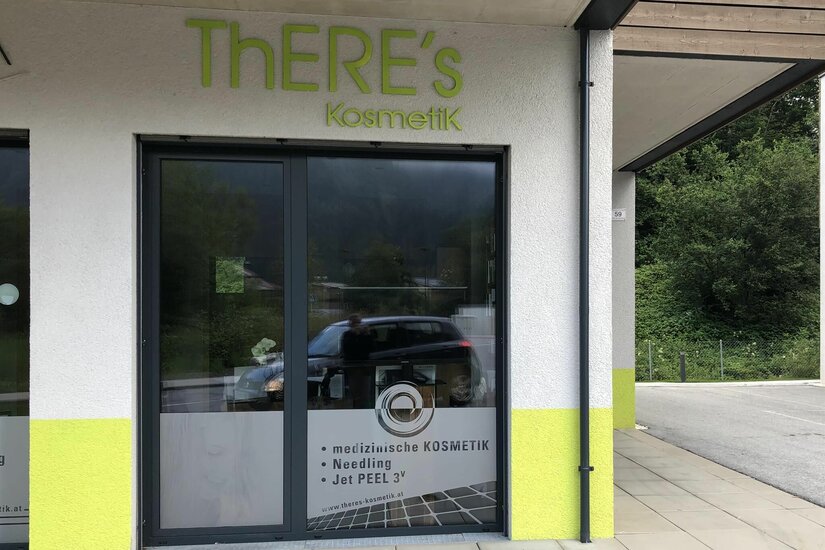 ThERE's Kosmetik Eingang Eingangsbereich von ThERE's Kosmetik mit Glasfront und grünem Schriftzug an der Fassade.