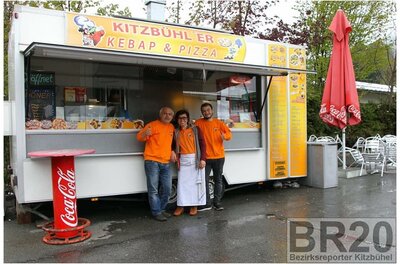 Kitzbühler Kebap & Pizza Ein Kiosk in Kitzbühel, der Kebap und Pizza verkauft. Drei Personen in orangefarbener Kleidung posieren freundlich vor dem Verkaufsstand.