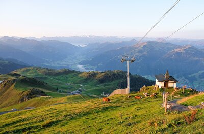 Eine malerische Berglandschaft mit sattem Grün und einer Seilbahn. Im Hintergrund sind die Berge und der Himmel zu sehen.
