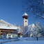 Verschneite Winterlandschaft in Aurach mit Kirche und traditionellen Holzhäusern unter blauem Himmel.