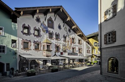 Fassade des Hotels Goldener Greif mit Wandmalereien und Außengastronomie in einer gepflasterten Gasse.
