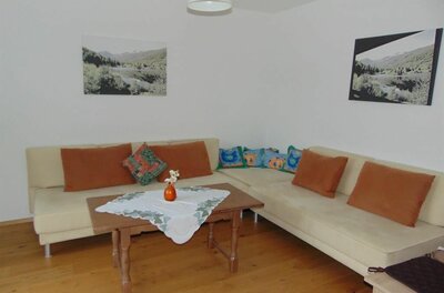 Wohnzimmer mit Ecksofa, Holztisch und Landschaftsbildern an weißen Wänden.