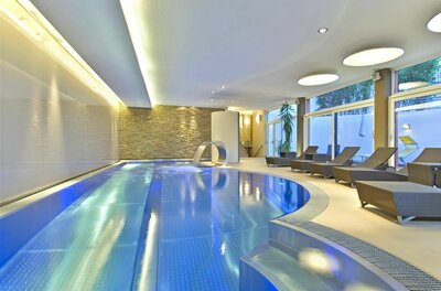 Wellnessbereich Aktivhotel Schweizerhof Modernes Hallenbad mit blauem Wasser, Schwalldusche und Ruheliegen im Innenbereich.