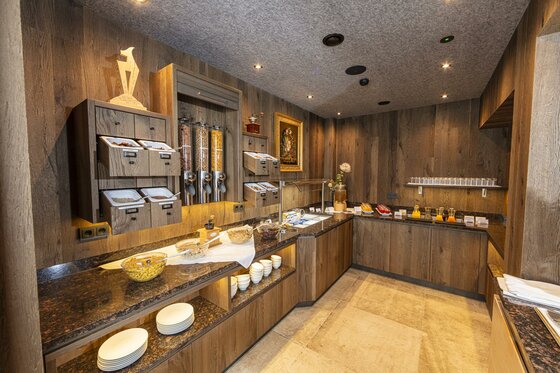 ©MartinRaffeiner_07_2024_RF_5091 <p>Ein elegantes Frühstücksbuffet mit Holzwänden und gedämpfter Beleuchtung. Auf den Tischen befinden sich verschiedene Lebensmittel.</p>