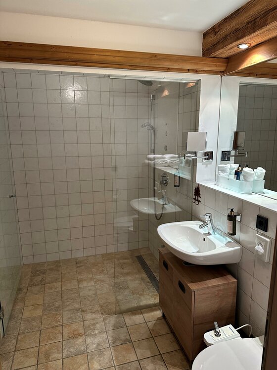 Apartment Ein modernes Badezimmer mit einer Duschkabine und einem Waschbecken. Die Wände sind gefliest und es gibt Holzdetails.