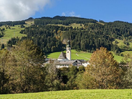 Pfarrkirche Jochberg am Museumsweg Blick auf die Pfarrkirche Jochberg vor bewaldetem Berghang unter blauem Himmel.