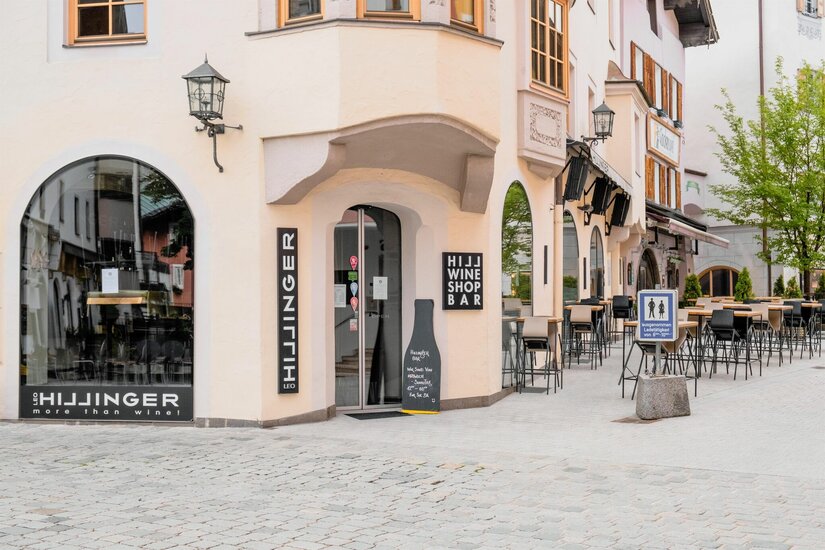Außenansicht einer Weinbar mit Tischen und Stühlen in einer gepflasterten Fußgängerzone.