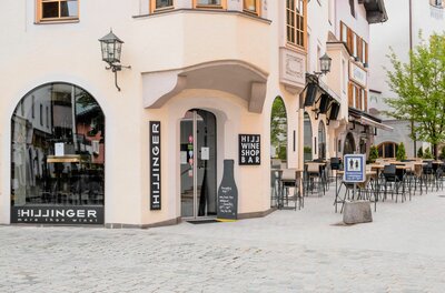 Leo Hillinger Weinshop und Bar Außenansicht einer Weinbar mit Tischen und Stühlen in einer gepflasterten Fußgängerzone.