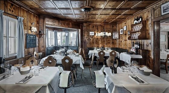 Sonnbühel Innenansicht Rustikale Gaststube mit holzgetäfelten Wänden, eingedeckten Tischen und traditionellen Holzstühlen.