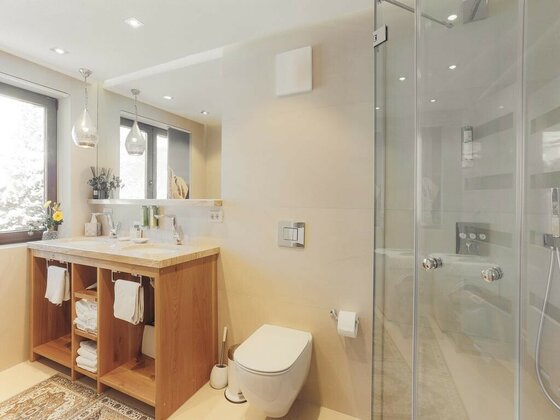 Badezimmer App Streifblick Modernes Badezimmer mit Holzwaschtisch, weißem WC und einer Glasdusche.